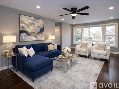 A living room with a blue sofa, two white armchairs, and a painting on the wall.