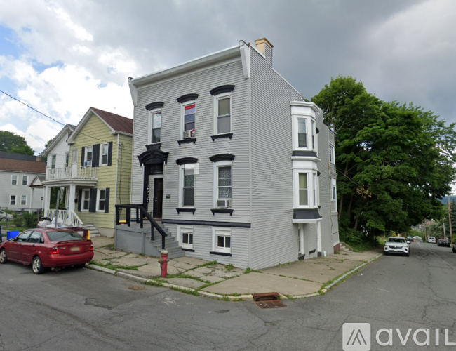 A grey two story house with a red car parked in front.