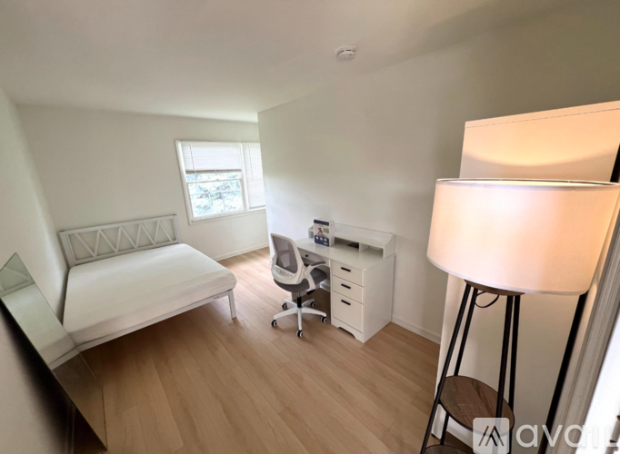 A well-lit room with a bed, desk, and chair.