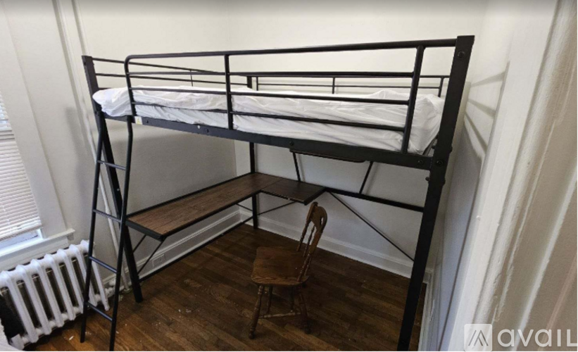 A black metal bunk bed with a white mattress and a wooden chair.
