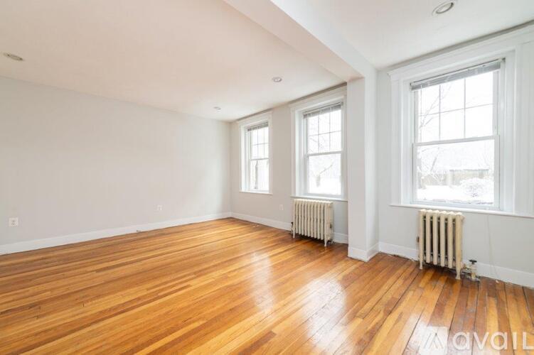 A room with wooden floors and white walls has two windows and two radiators.
