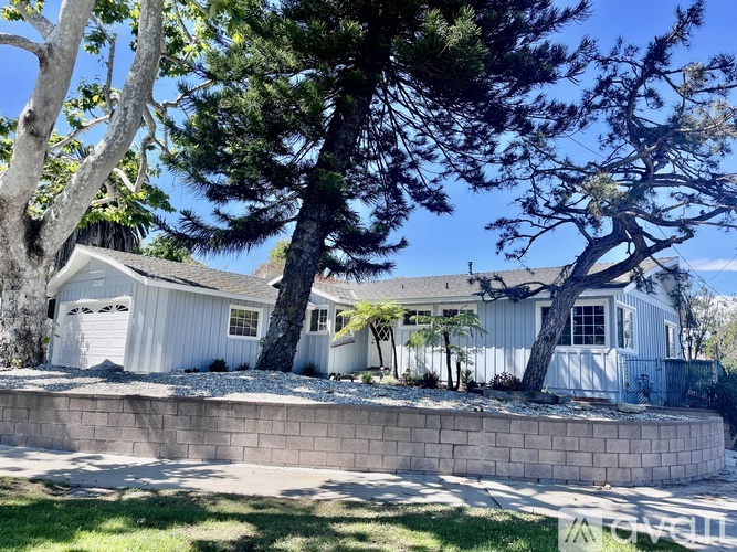 A house with a white exterior and a grey roof is surrounded by trees.