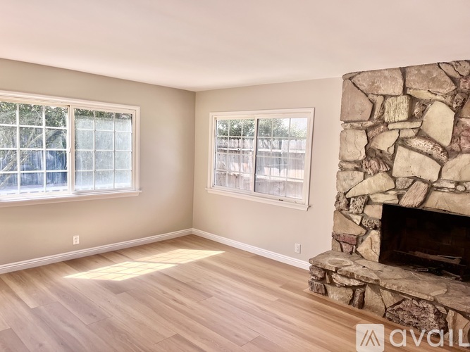 A room with a stone fireplace and two windows.