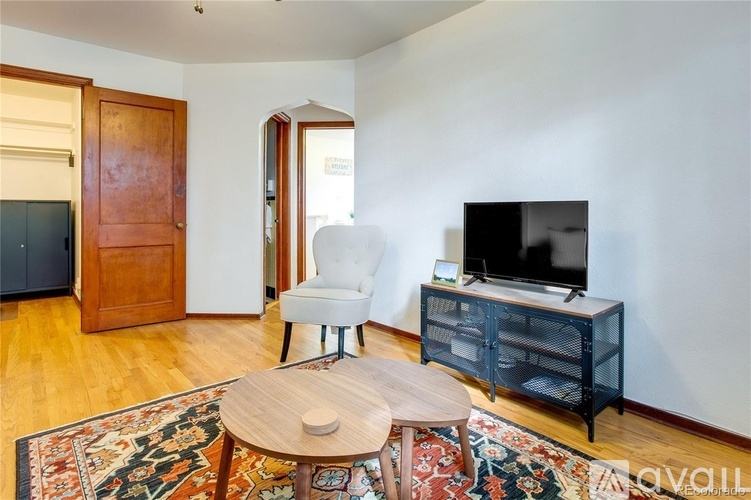 A living room with a wooden floor, a white chair, a wooden coffee table, a television, and a cabinet.