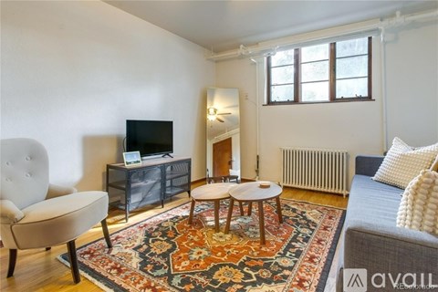 A living room with a white chair, a white ottoman, a white couch, a white rug, a white wall, a white ceiling, a white floor, a white door, a white window, a white table, a white television