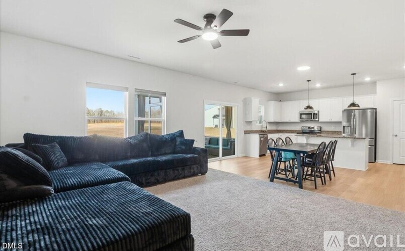 A living room with a dark blue sofa and a dining area with a table and chairs.