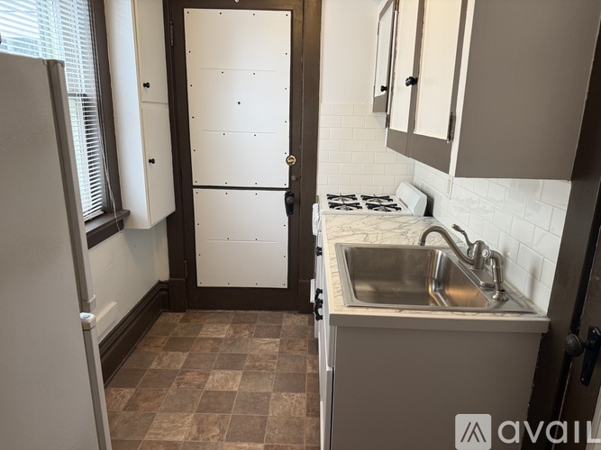 A kitchen with a white fridge, sink and brown tiles.