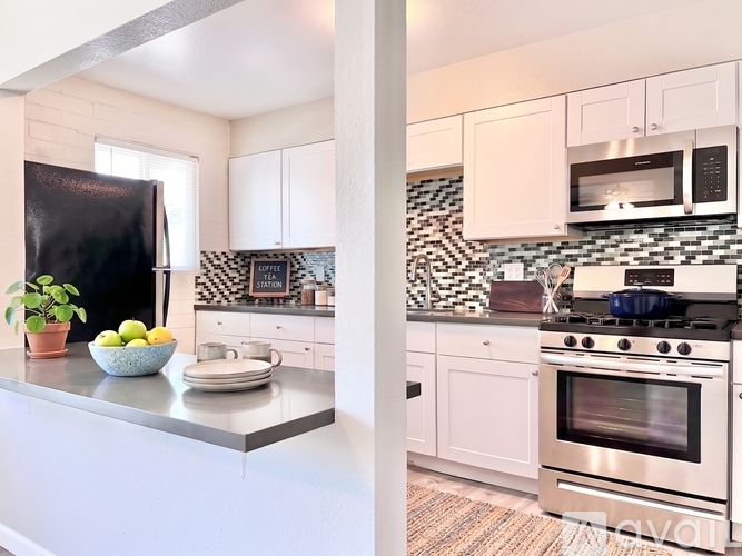 A kitchen with a black fridge, white cabinets, and a black and white checkered backsplash.