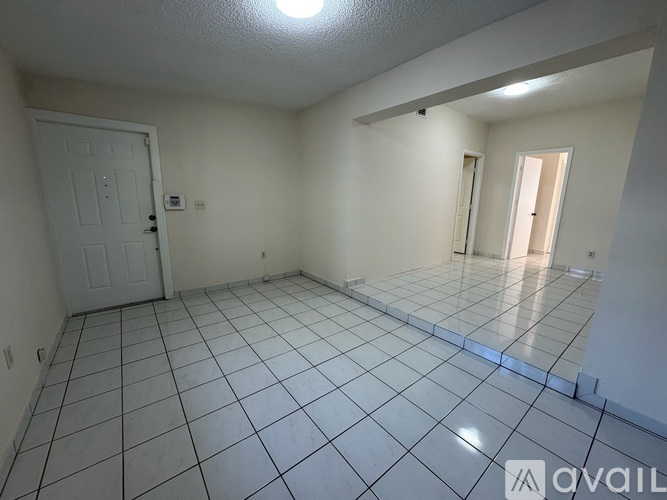 A spacious room with white tile flooring and a door on the left.