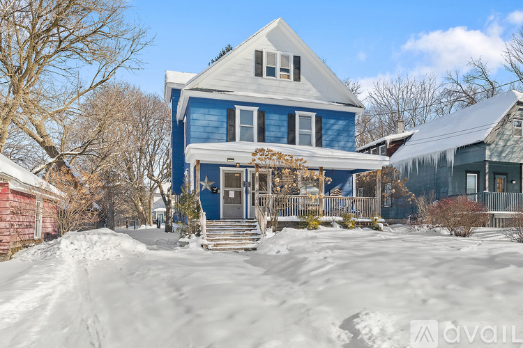 A blue house with a white roof and a porch covered in snow.