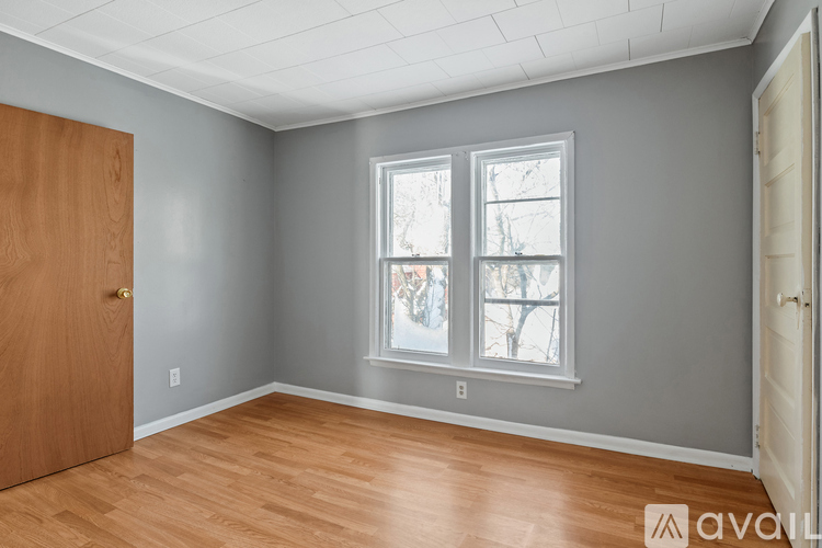 A room with a wooden floor, grey walls, a window with a view of trees outside, and a door on the left.