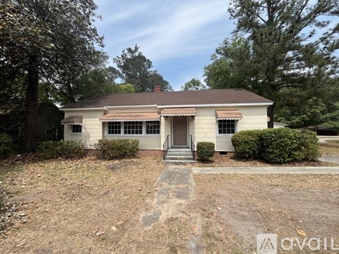 A house with a brown roof and a white front is surrounded by trees and bushes.