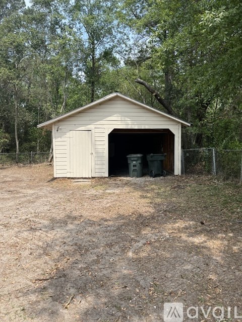 A shed with a brown roof and white walls is in a grassy area with trees in the background.