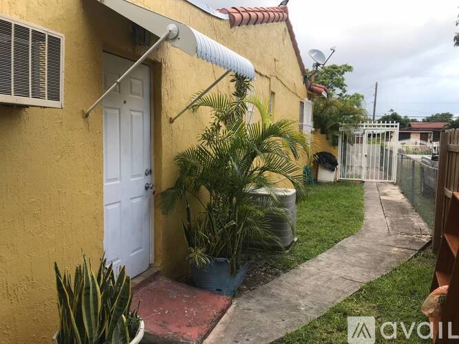 A yellow house with a white door and a red brick walkway.