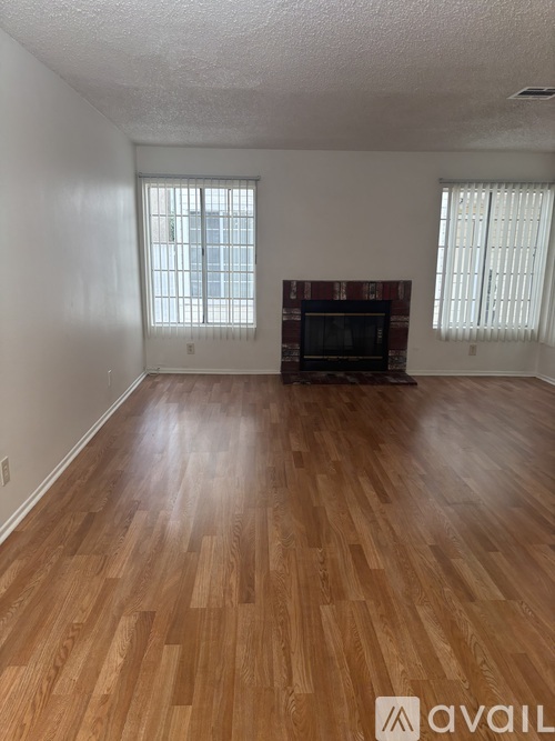 A room with wooden flooring and two windows.