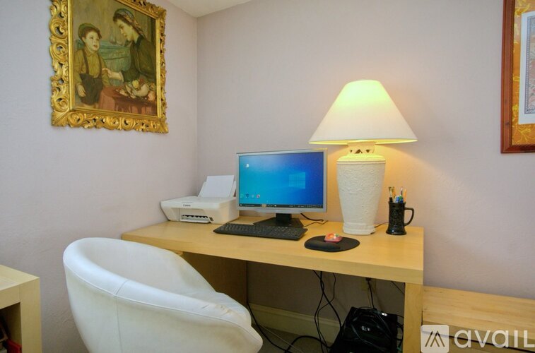A desk with a computer, monitor, keyboard, and mouse is set up in a room with a painting on the wall.