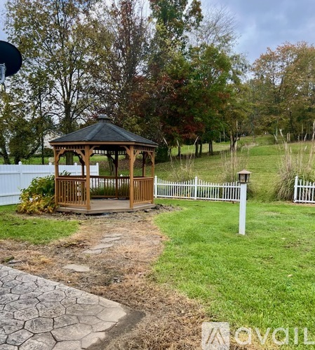 A gazebo sits in a grassy area with a white picket fence.