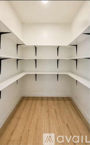 Empty walk-in closet with wooden floors and white shelves.