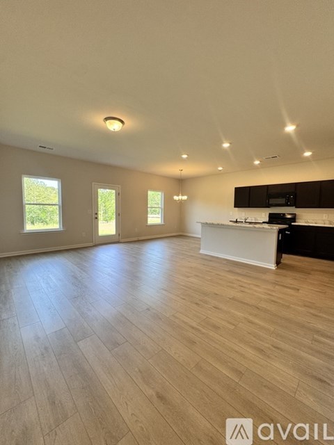 A spacious room with wooden flooring and a kitchen area.