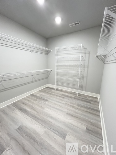 A spacious walk-in closet with wooden flooring and white shelving.