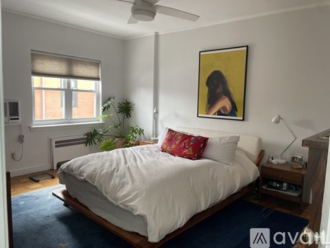 A bedroom with a bed, a ceiling fan, and a painting on the wall.