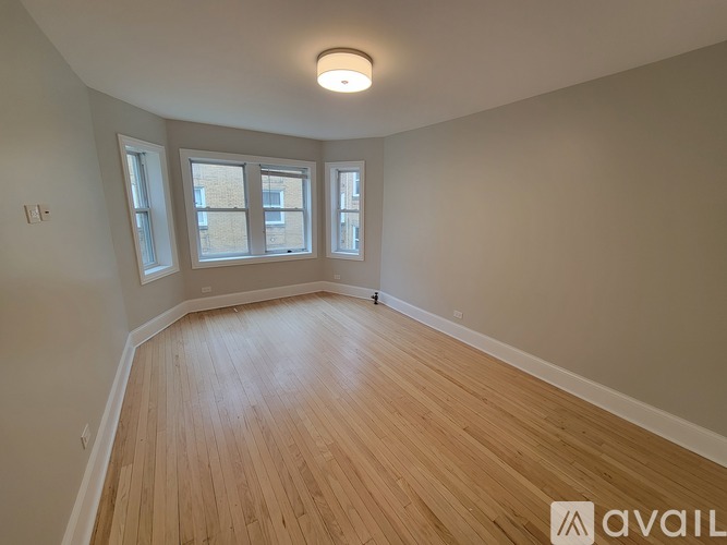 A room with wooden flooring and three windows.