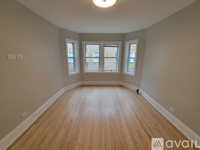 A room with wooden flooring and three windows.