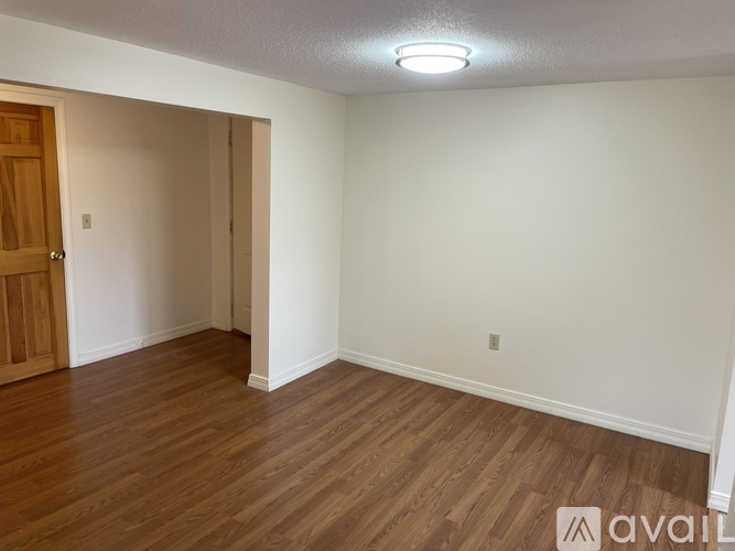 A room with wooden floors and a white wall with a door on the left side.