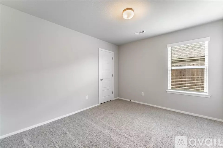 A room with a carpeted floor, a door, and a window with blinds.