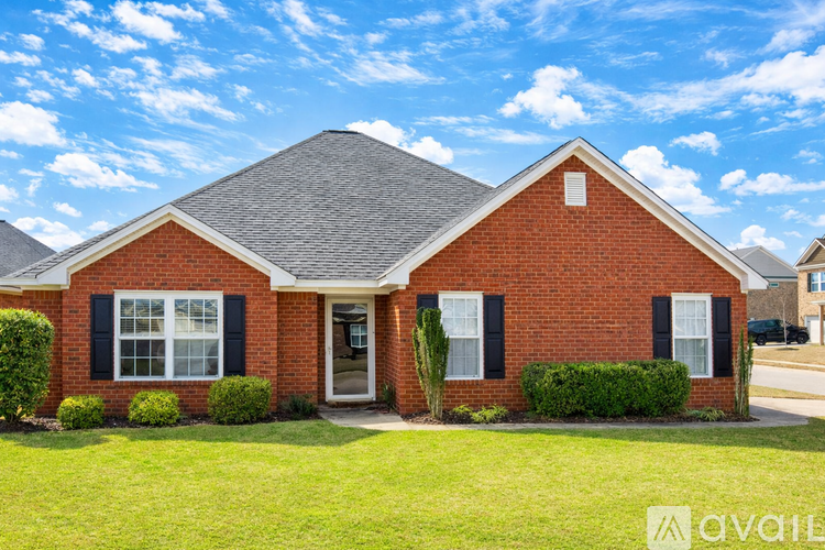 A red brick house with a grey roof and a green lawn in front.