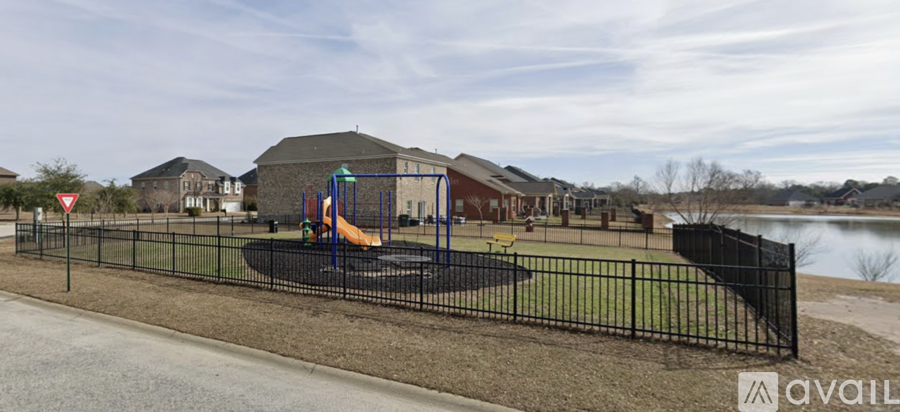 A playground with a slide and a trampoline is enclosed by a black fence.