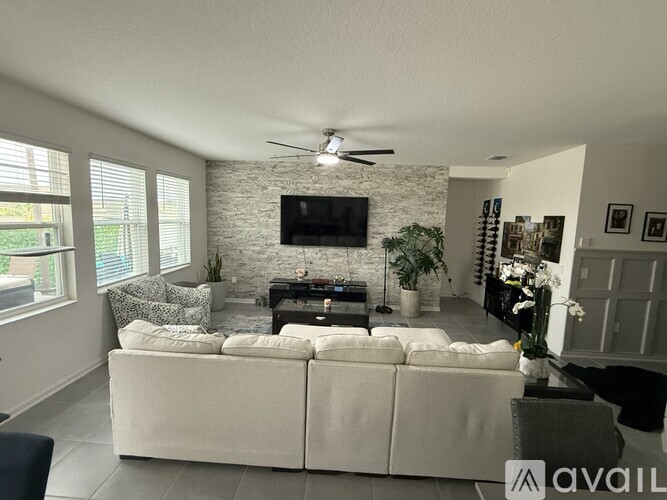 A living room with a white couch and a flat screen TV mounted on the wall.