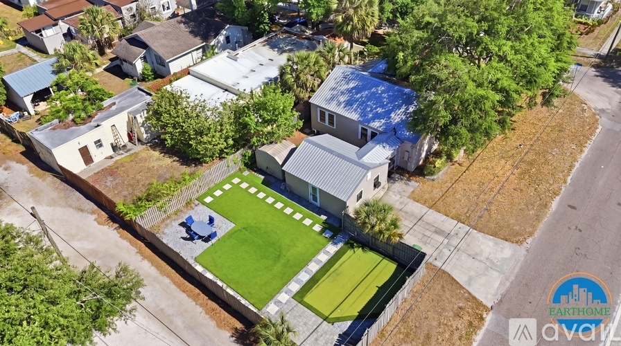 A house with a blue roof is surrounded by a fence and has a green lawn.