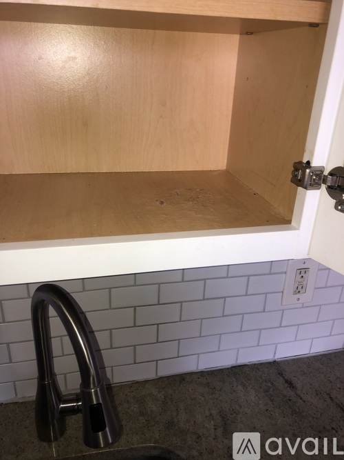 A kitchen cabinet with a white tile backsplash and a black faucet.