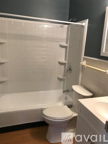 A white toilet sits in a bathroom with a white tiled shower.