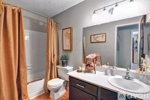 A bathroom with a white toilet, a sink, and a shower with orange curtains.