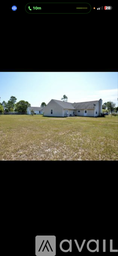 A white house with a grey roof is situated in a grassy field.
