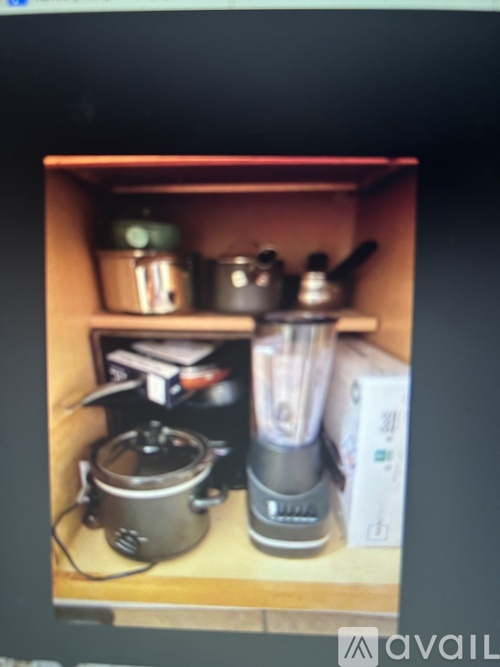 A kitchen cabinet with a pot, a blender, and a toaster.