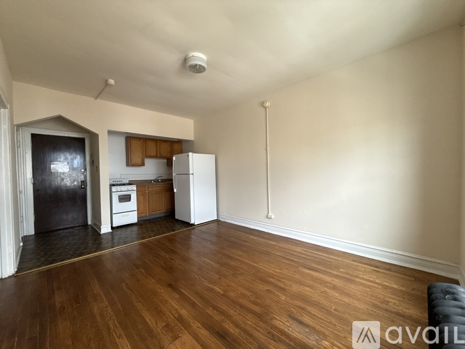 A spacious room with wooden floors and a kitchen area in the background.