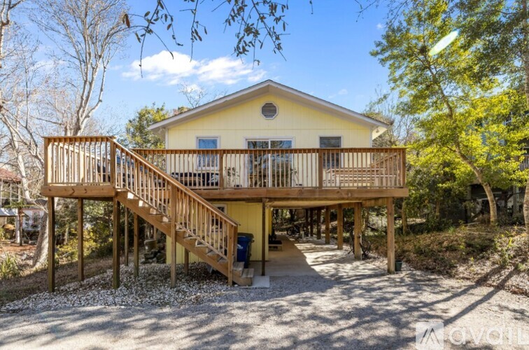 A yellow house with a wooden deck and stairs leading to the front door.