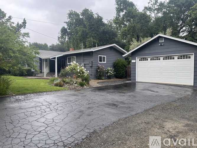A house with a grey garage door is surrounded by greenery.