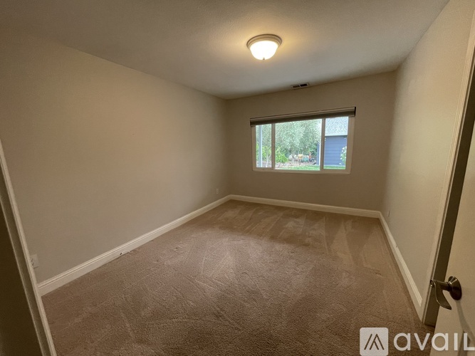A room with a carpeted floor and a window showing a view of trees and a fence.