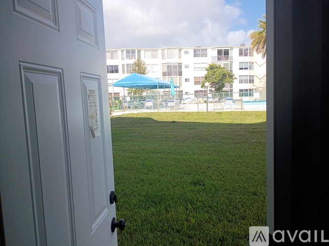 A view from a door looking out to a grassy area with a pool and apartment building in the background.