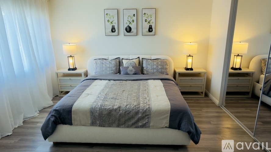 A bedroom with a large bed, two nightstands with lamps, and framed pictures on the wall.