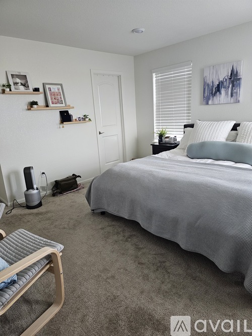 A bedroom with a bed, chair, and a wall-mounted shelf with picture frames and plants.