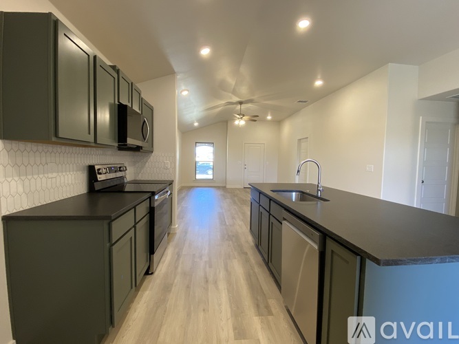 A modern kitchen with dark green cabinets and a wooden floor.