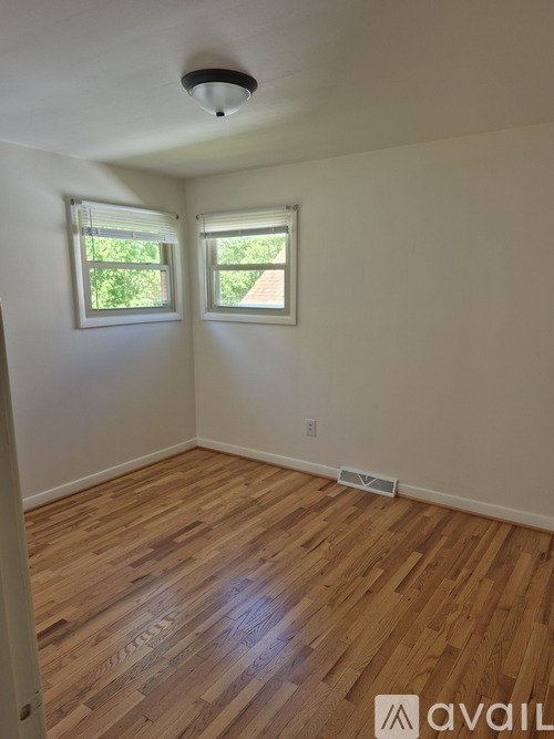 A room with wooden flooring and two windows.