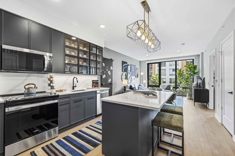 A modern kitchen with dark cabinets and a marble countertop.