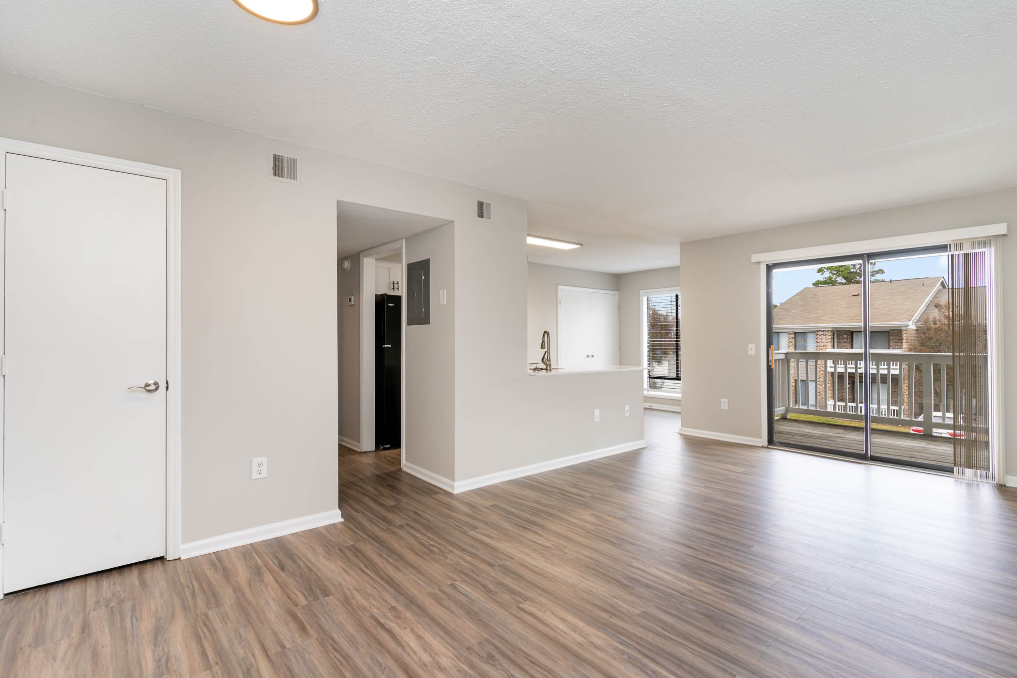 A spacious living room with wood flooring and a view of a house through the glass door.