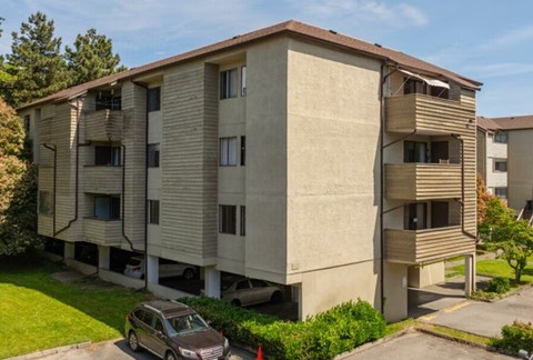 A car is parked in front of a tan apartment building.